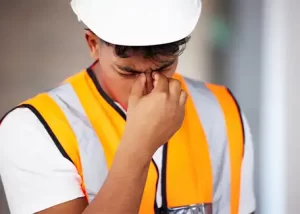 Stressed construction worker wearing a reflective safety vest and white hard hat