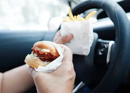 Person eating a fast food burger and fries while driving a car