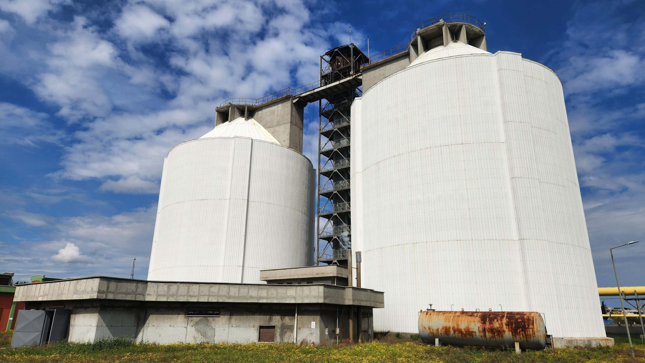 A low-angle view of two massive white industrial fermentation tanks and a central steel service tower, showcasing the large-scale infrastructure supported by strategic biogas procurement.